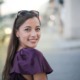 Cheerful woman in a purple top smiles at the camera on a bustling city street.