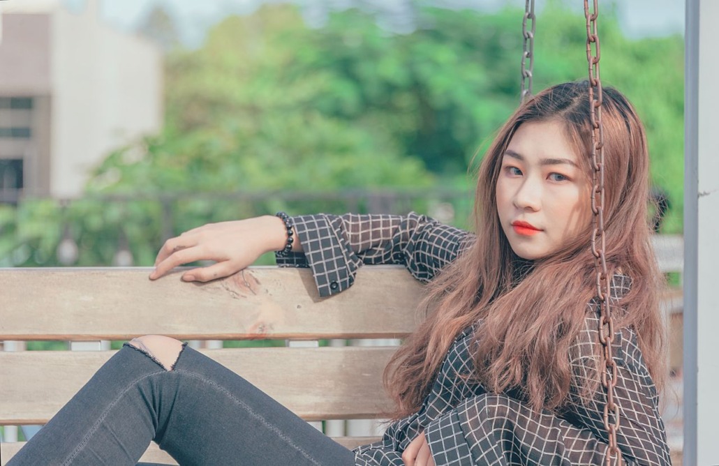 Stylish young woman sitting on an outdoor swing in casual attire on a sunny day.