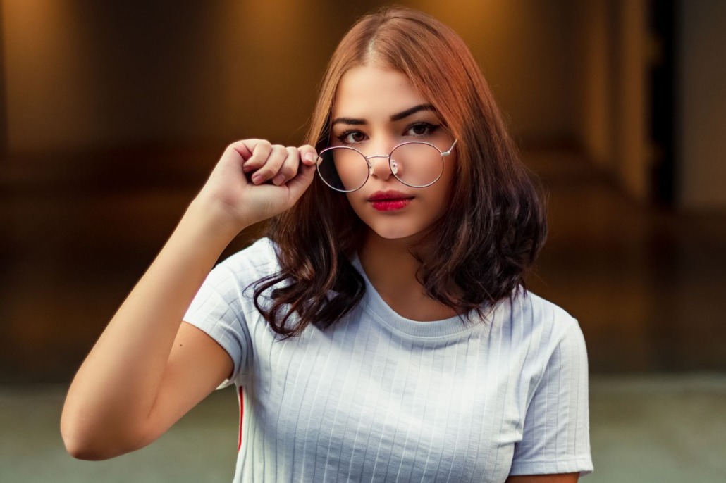 Portrait of a stylish young woman adjusting her eyeglasses indoors, exuding confidence and elegance.
